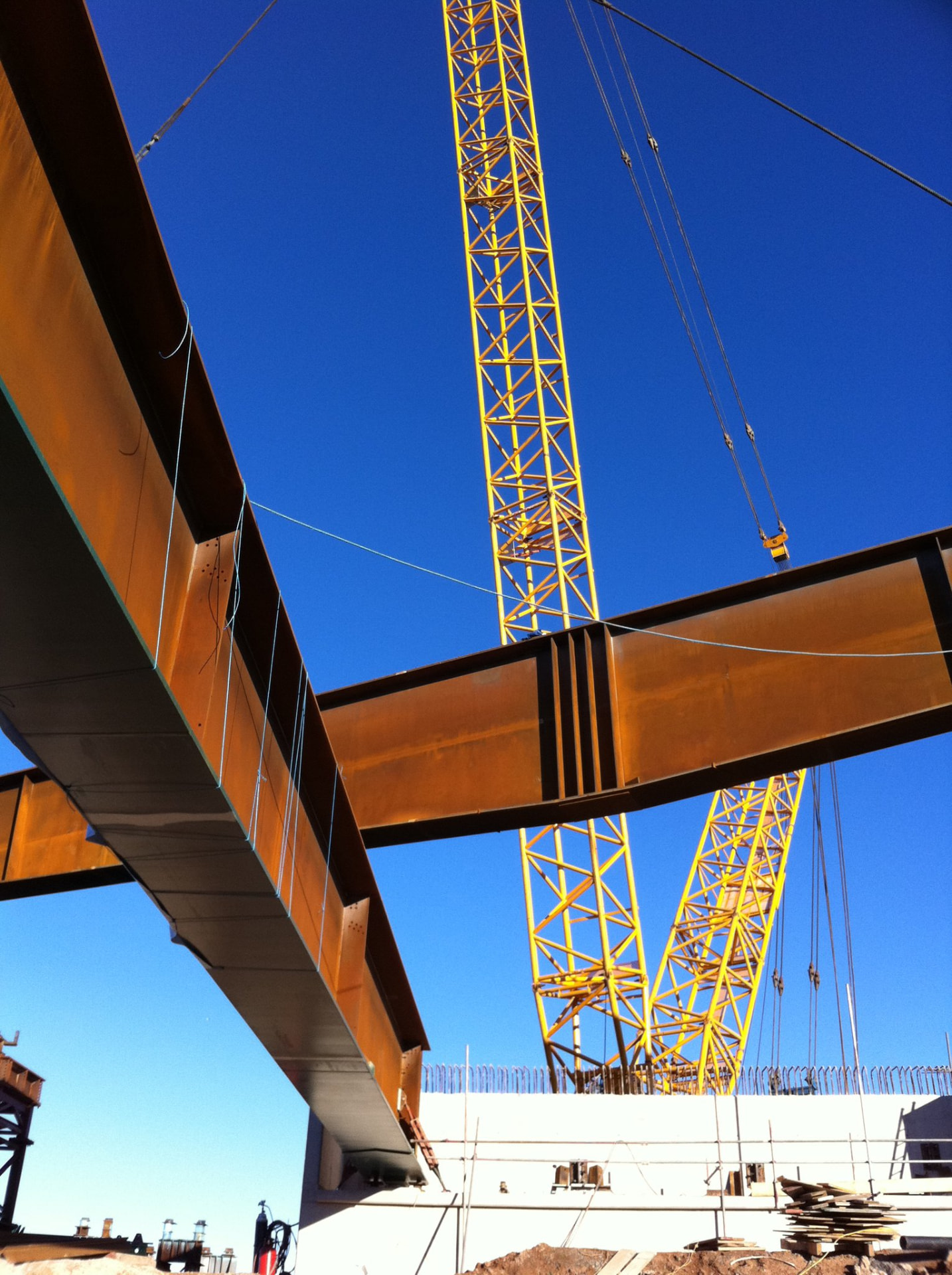 Yellow lattice crane lifting steel bridge beams against a clear blue sky